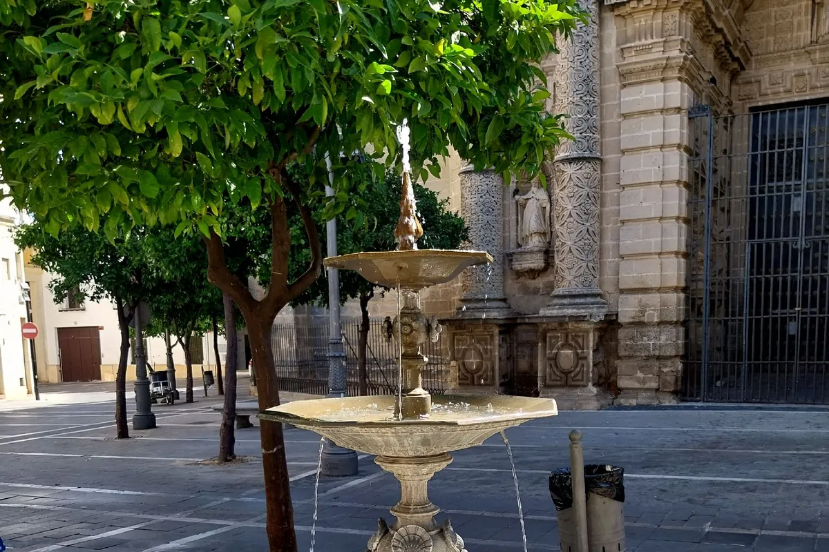 Kamenná fontána s vyřezávanou nádrží na Plaza de San Miguel v Jerezu, za ní pomerančovníky a vchod do kostela